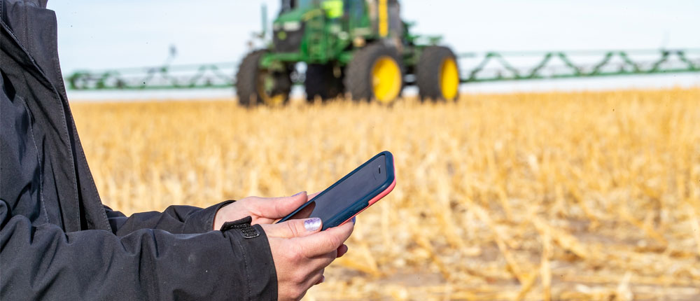 Hands holding a smartphone with a harvested field in the background