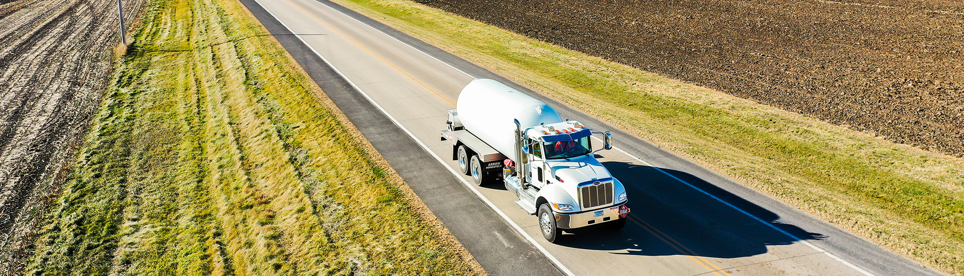 Propane delivery truck on open road between two fields